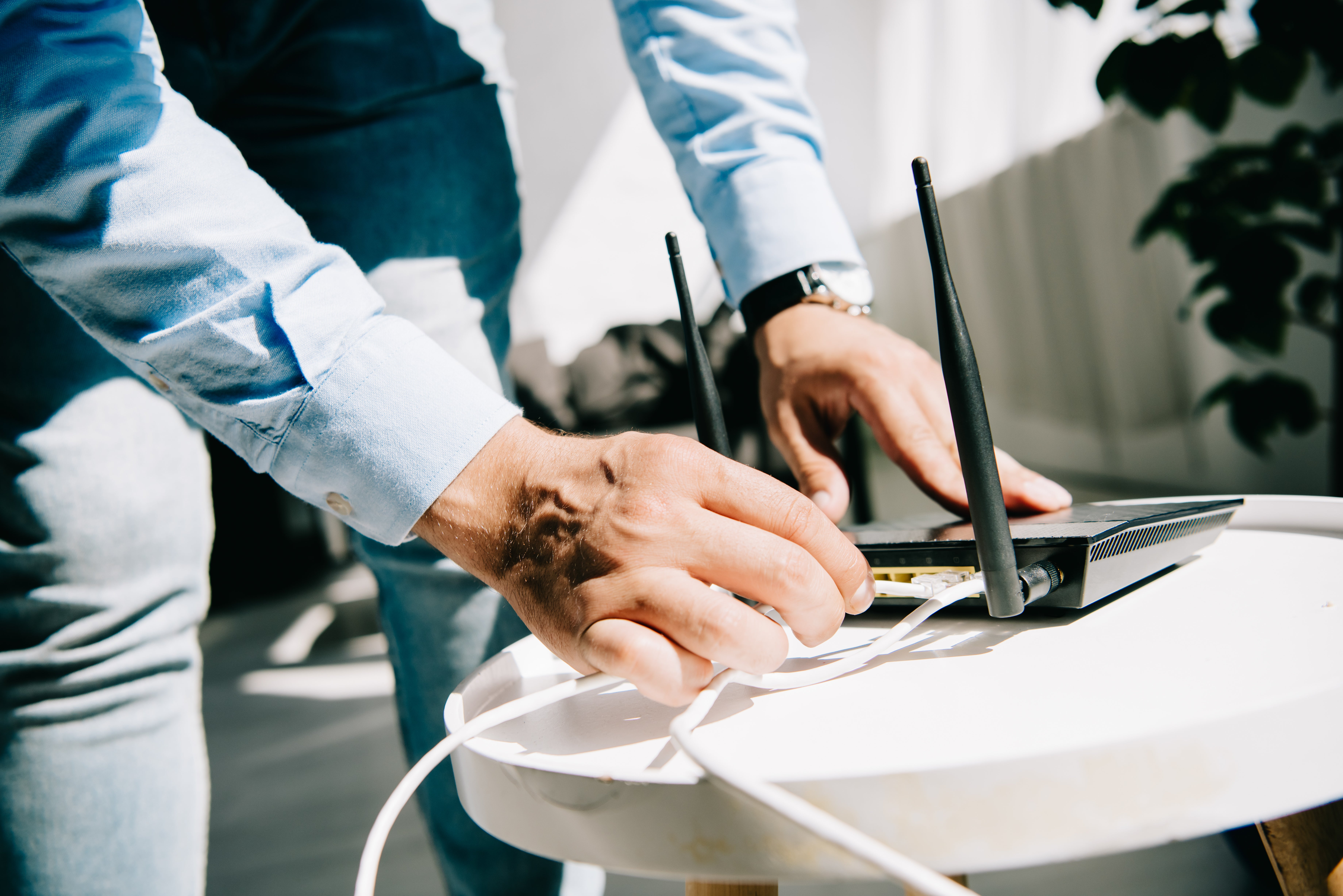 Person connecting cables to a wireless router during home internet troubleshooting. Close-up image of router setup and network equipment used to restore or improve residential broadband and Wi-Fi service.